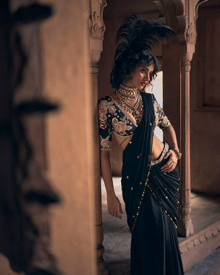 A close up look of the black pre–stitched cocktail saree, hand–embroidered in delicate floral motifs and lace detailing, evoking the charm of a bygone era. The pallu features metal sequin work and floral buttis. It is paired with a signature Paulmi and Harsh printed blouse with rose gold embroidery and a hand-embroidered belt.