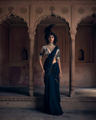 A romantic black pre–stitched cocktail saree, hand–embroidered in delicate floral motifs and lace detailing, evoking the charm of a bygone era. The pallu features metal sequin work and floral buttis. It is paired with a signature Paulmi and Harsh printed blouse with rose gold embroidery and a hand-embroidered belt.