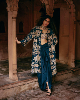 A blue jacket hand-embroidered in zardozi, sequins and baby flowers in Paulmi and Harsh signature Roop flip bird print, featuring a pair of birds in their enchanting habitat. It is paired with a intricately hand-embroidered scallop detailed blouse with scattered butti detailing and a solid pre–draped knot detailed skirt.