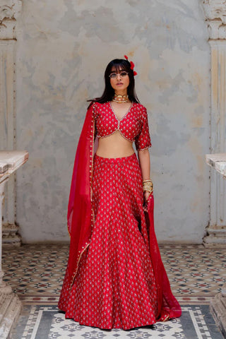 Featuring a cherry red silk hand block printed and embroidered blouse with scallop embroidered neckline. It is paired with a matching silk fit waist lehenga with pockets and comes with a cherry red silk organza dupatta with sequins booti border and gota lace edging on all sides. Designed by Ivory by Deepika