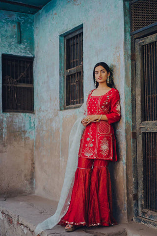 Featuring a cherry red short kurta in raw silk base with floral hand embroidery paired with matching kota doria gharara having gold zari weave. It comes with an aqua block printed dupatta in silk organza base.