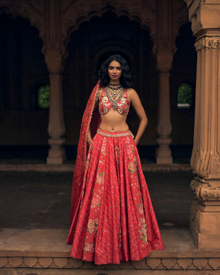 An ethereal crimson lehenga in a combination of floral, leheriya and abstract floral prints, with delicate zardozi and aari hand-embroidery, and an embroidered attached belt. It is paired with a hand-embroidered floral Paulmi and Harsh signature blouse, and a scallop hand-embroidered dupatta.