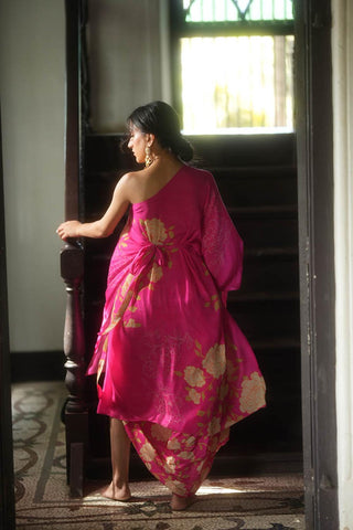 Back look of A rani pink gorgeous rose print draped one shoulder tie up dress, paired with an all–over printed cowl skirt designed by Paulmi and Harsh. 