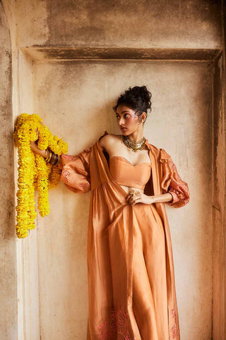 Designed by Paulmi and Harsh the peachy orange jacket set crafted in pure silk organza fabric and has a cutwork embroidery details as a design element. The jacket set has volumious sleeve details. The set includes bustier and straight fit trouser.  An Indo-Western women clothing a beach wear, party, summer wear, dinner date, evening dress to flaunt and style.