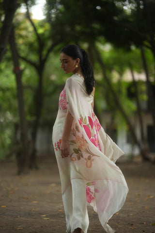 Back look of a rose and anar placement print one shoulder dress with coin detailing on the neck, paired with off–white pants designed by Paulmi and Harsh. A perfect dress for vacation, holiday, beach, casual, lunch party, girls day out wear.