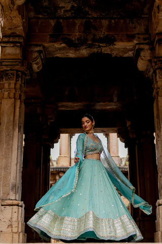 Featuring a sky blue embroidered flared lehenga in zari tissue base with zari, pearls and sequins embroidered thick border. It is paired with a matching hand embroidered blouse in tissue base with deep V-neckline and elbow length sleeves. It comes with a sky blue coloured silk organza dupatta with gota lace border on all sides.