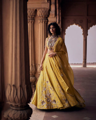 A tuscany yellow hand-embroidered lehenga set, featuring ornate aari and zardozi embroidery, in alternating kalis of chintz and small floral buttis. It is paired with a hand-embroidered dupatta, featuring floral bunches and double scallop embroidered borders.